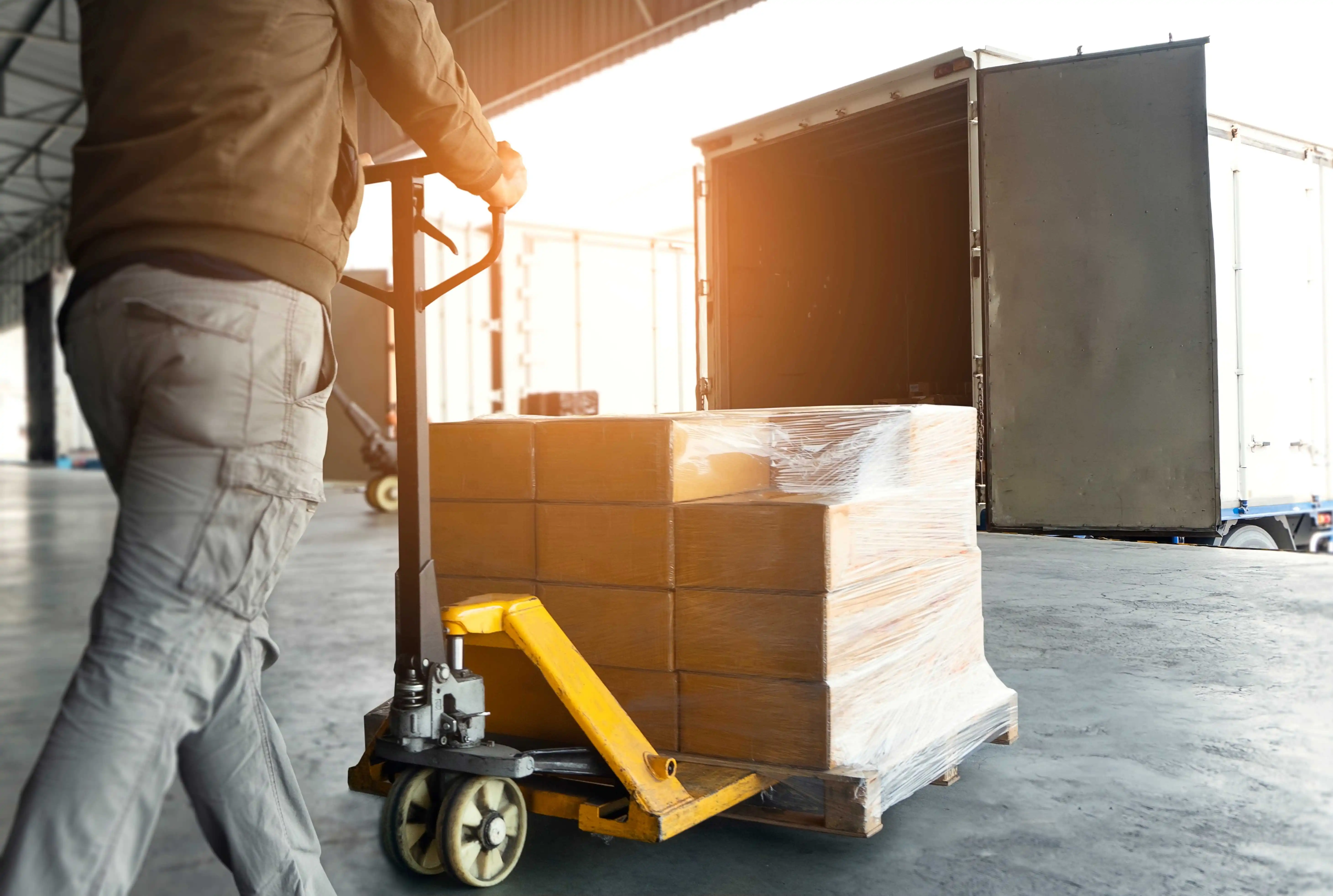 A male courier using a pallet jack to move a pallet of cartons