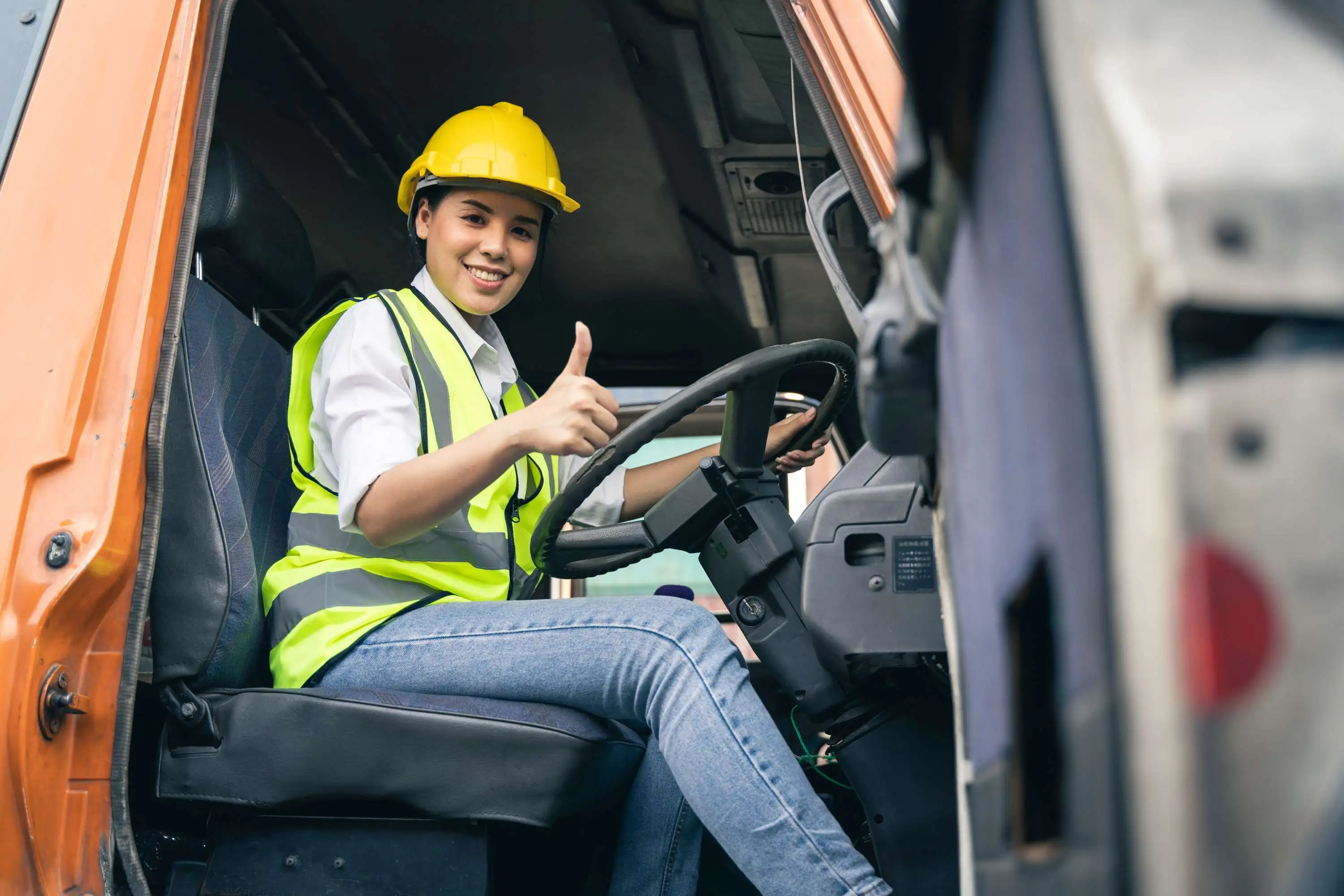 A female truck driver poses from the driver seat of her truck